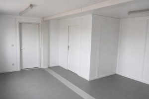 Innenansicht eines ungemöblierten Standard-Wohncontainers mit einfachem Bodenbelag und Wandverkleidungen aus Spanplatten