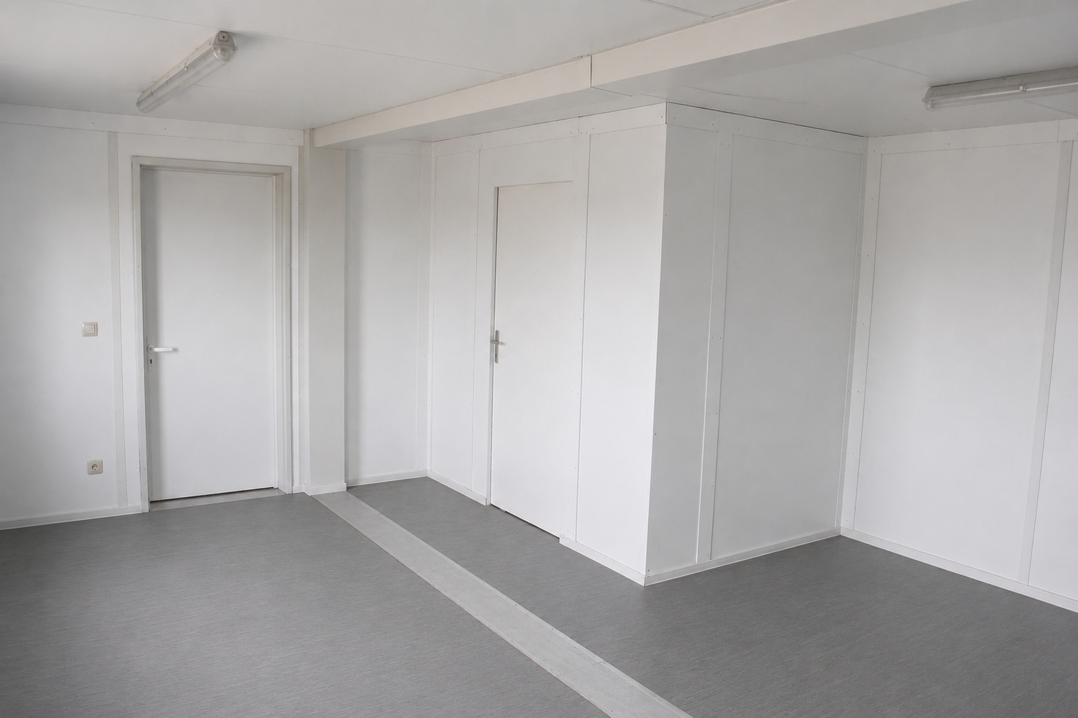Innenansicht eines ungemöblierten Standard-Wohncontainers mit einfachem Bodenbelag und Wandverkleidungen aus Spanplatten
